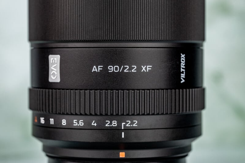Close-up of a black Viltrox camera lens showing the model "AF 90/2.2 XF" and aperture values from f/1 to f/16 on the focus ring.