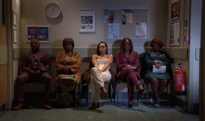 EastEnders Chelsea white From left to right, Howie Danes, Yolande Trueman, Chelsea Fox, Denise Fox, and Kim Fox sit in a hospital waiting room with a clock on the wall reading both hands at 1 in EastEnders.