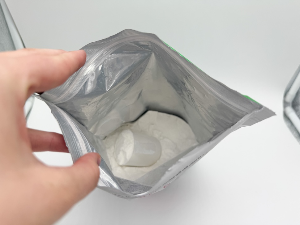 A hand opening a pouch of 1st Phorm Phormula-1 Clear. You can see the fine white powder inside, along with a small plastic scooper.