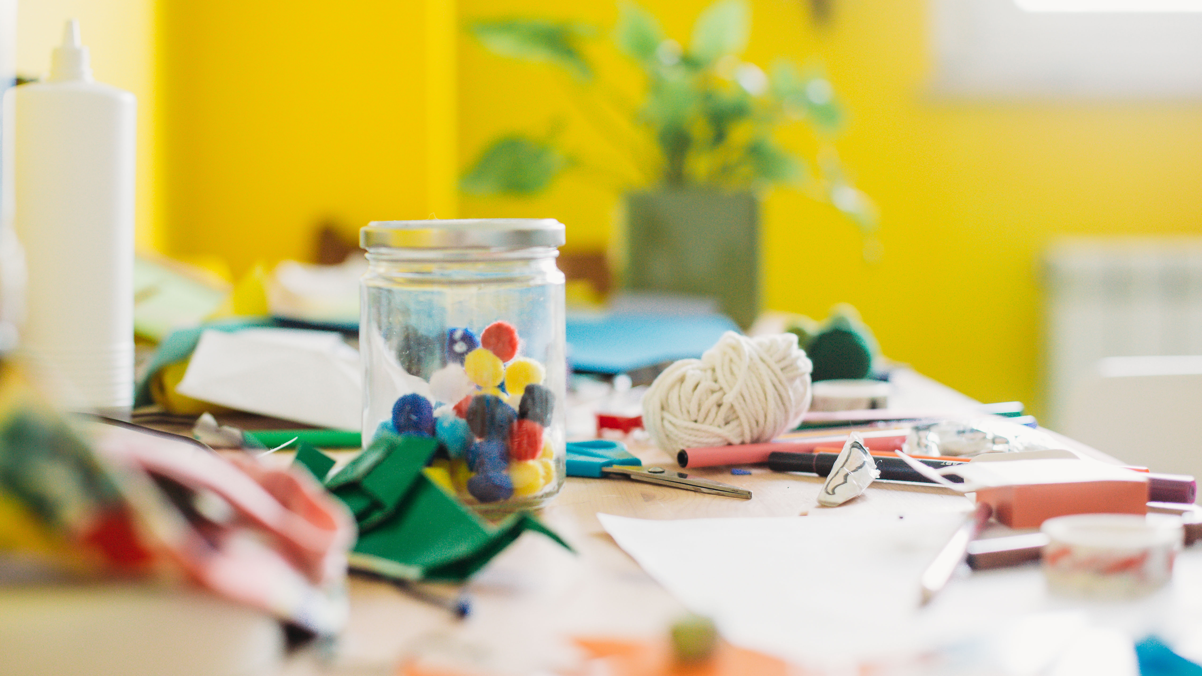 Jar with color pompoms on a messy desk full of craft supplies.