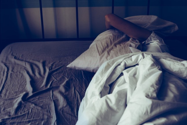A woman trying to sleep more, having trouble sleeping due to noise, covering her ears with pillow ...