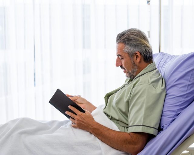 Caucasian mid adult patient writing a diary while recovering in the hospital ward - stock photo