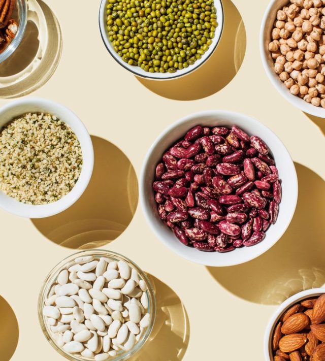 Various kinds of vegan protein sources on beige background. Set of food supplements. Gluten free cereals as ground hemp seeds, quinoa. Nuts and legumes (green mung beans, chick-pea, red lentil, kidney bean, almonds, hazelnuts). Flat lay, top view - stock photo