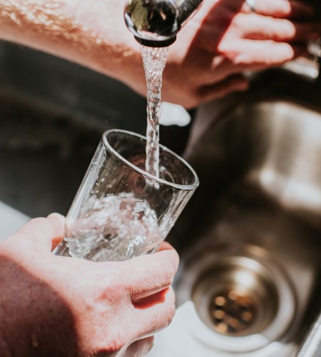 A man pours a glass of water from a chrome tap at a kitchen sink - stock photo