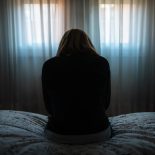 Woman sitting on the bed on her back with a depressive and tired attitude. - stock photo