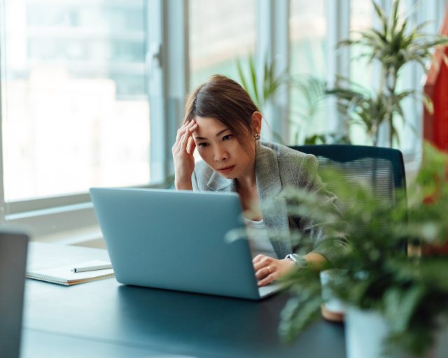 Tired Asian businesswoman working on a laptop computer in the office - stock photo
