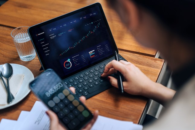Young Asian businesswoman managing personal finance and investment. Checking investment and stock market trades, making financial plans and setting financial goals with smartphone and digital tablet in cafe. Wealth management and online banking