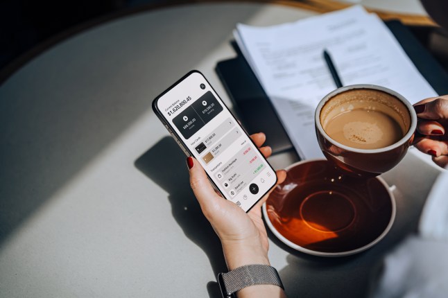 Cropped shot of a woman accessing online banking with mobile app on smartphone to manage her banking needs in a cafe. Managing finance and investment at easy access. Wealth management. Smart banking with technology