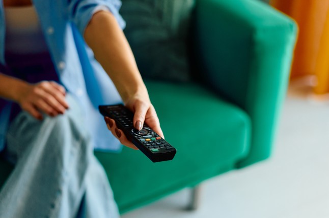 Woman holding remote control changing television channels at home