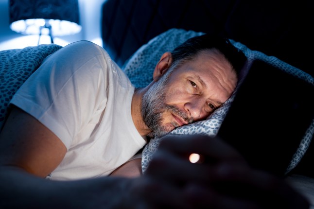 Man struggling with insomnia at night using smartphone in bed