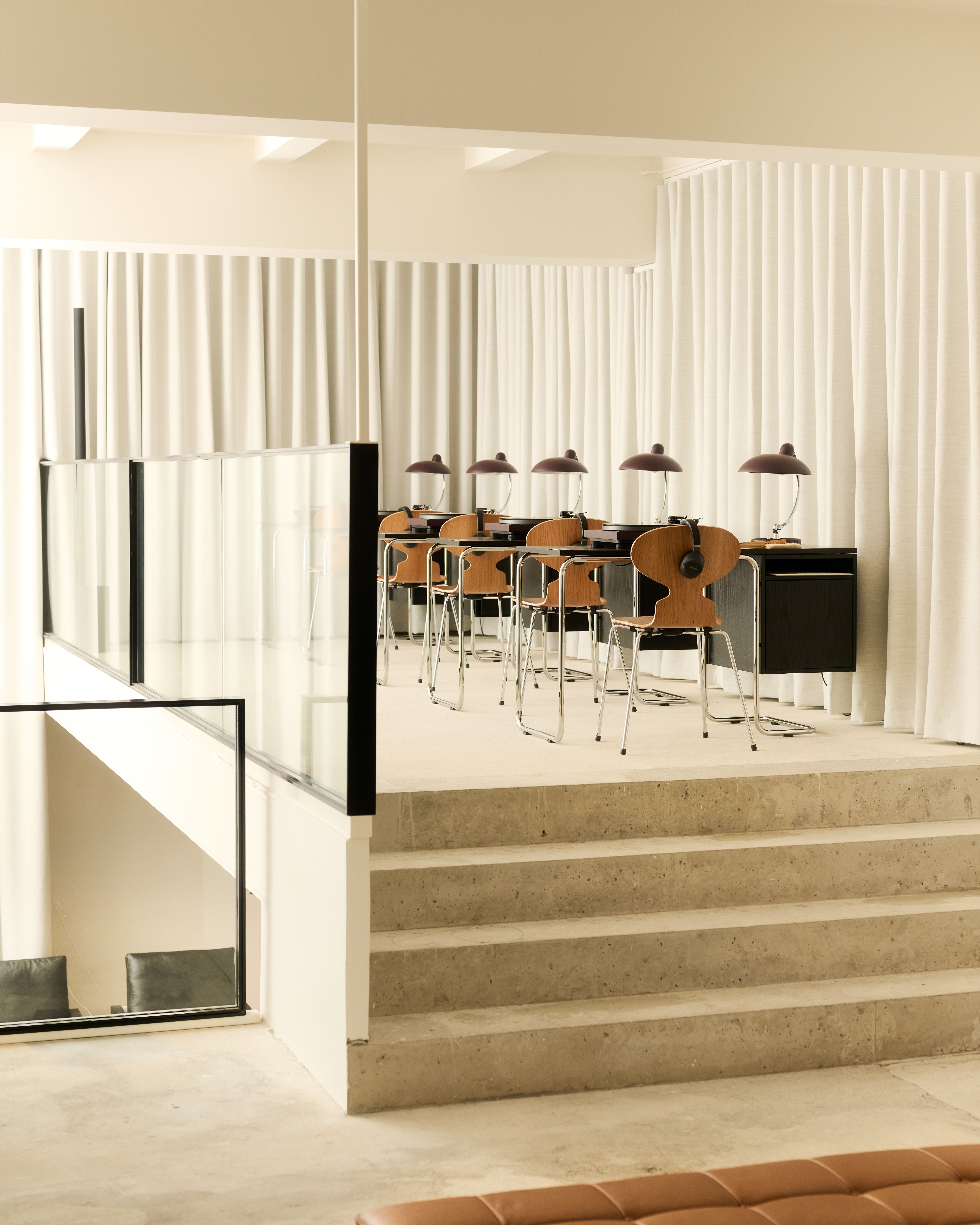 An audio-equipped showroom features cement architecture mixed with glass and iron details, wooden furniture, and mid-century modern desks with headphones, record players, and matching lamps.
