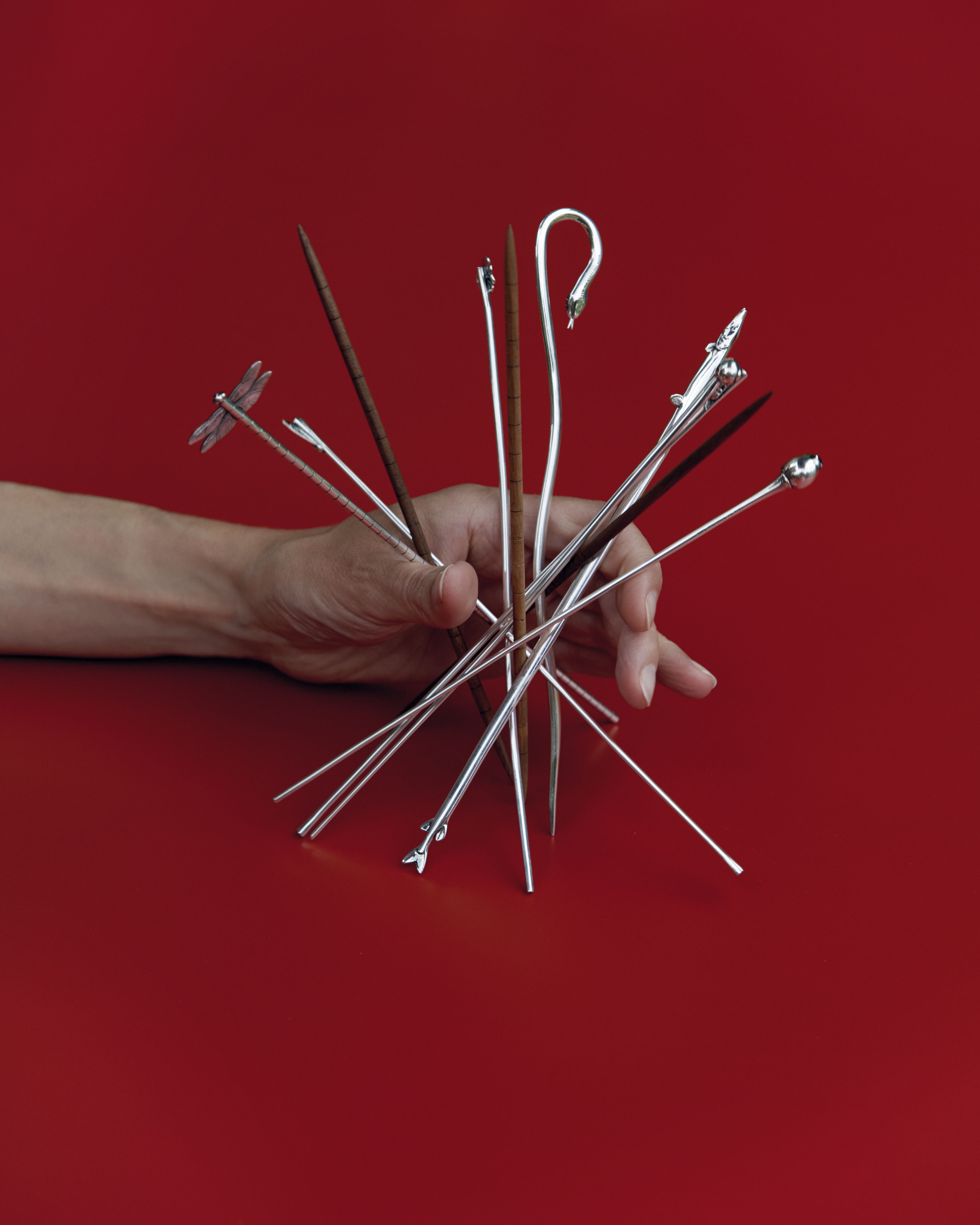 Hands handling some design games, including chrome-clad sticks, and straw and silver-made rings.