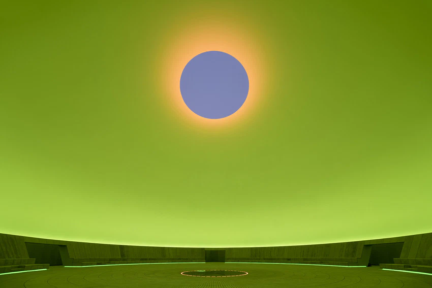 Wide view of a green-lit room with a circular seating area and a glowing circular ceiling light in the center.