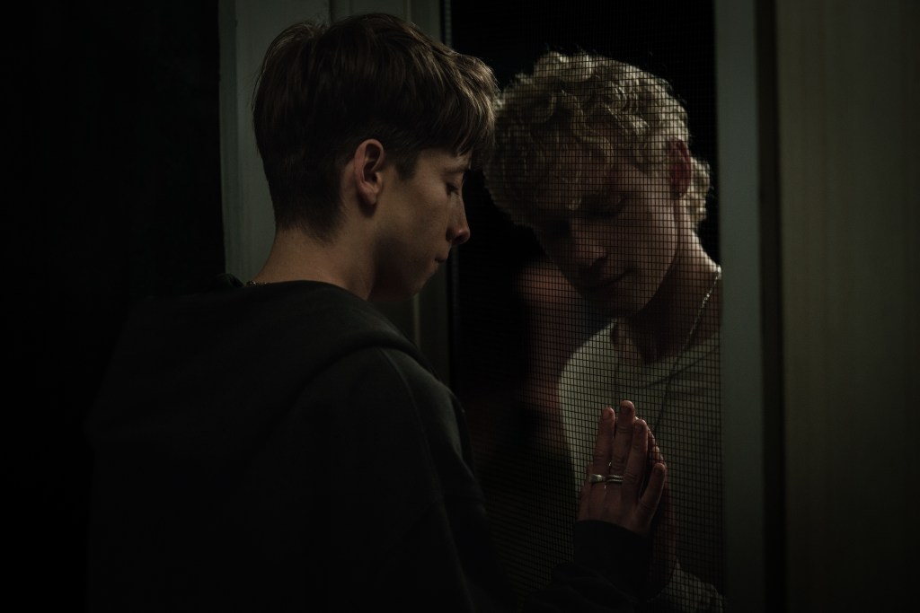 Leviticus still: two boys pressing their hands together but seperated by a netting window