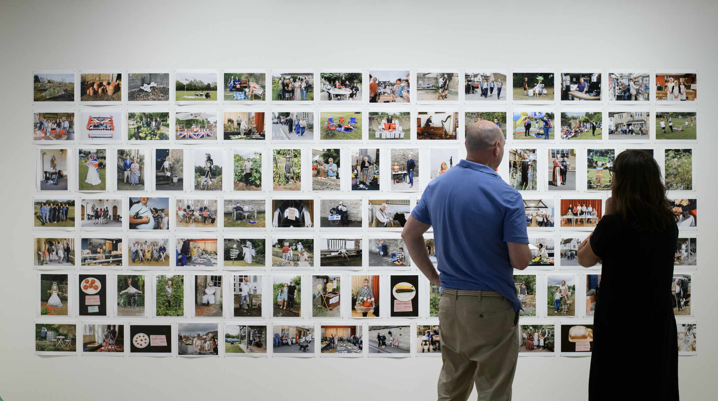 A man stands looking at a large wall covered in rows of small contact-sheet style prints from the Lacock project.