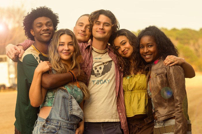 OBX_S5_Wrap_26834RC Jonathan Daviss as Pope, Madelyn Cline as Sarah Cameron, Drew Starkey as Rafe, Chase Stokes as John B, Madison Bailey as Kiara and Carlacia Grant as Cleo in Outer Banks season 5, with their arms around each other and smiling at the camera.