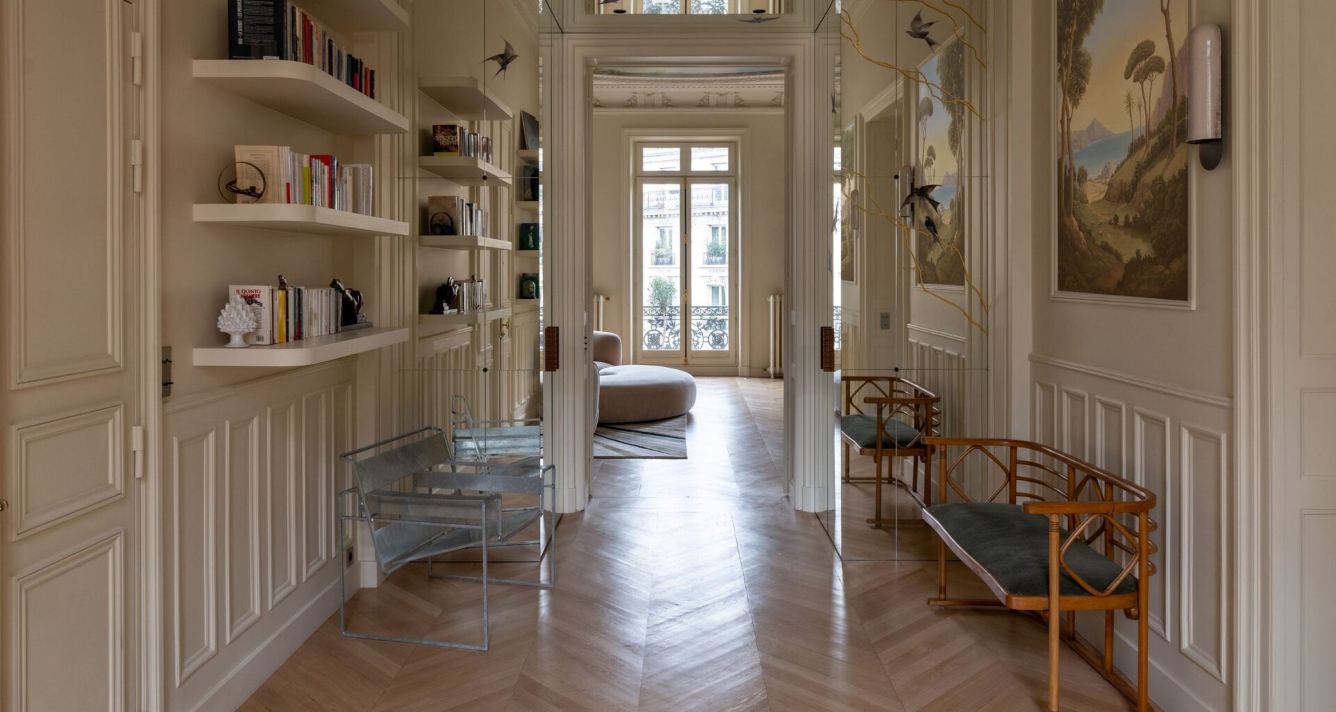 A grand hallway with off-white walls, paneling, and open shelving with seating benches along either side of the walls and paintings along the right-hand side