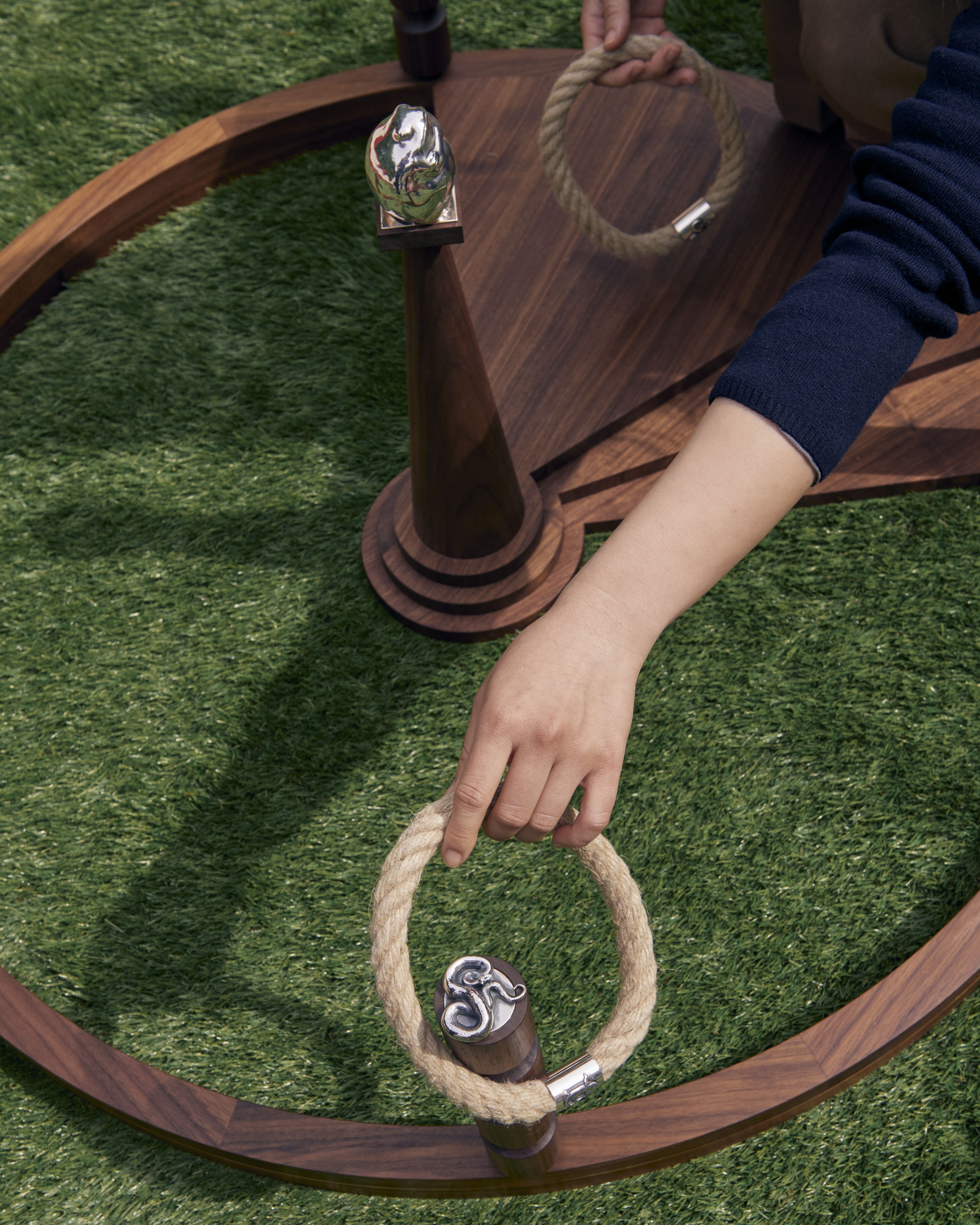 Hands handling some design games, including chrome-clad sticks, and straw and silver-made rings.