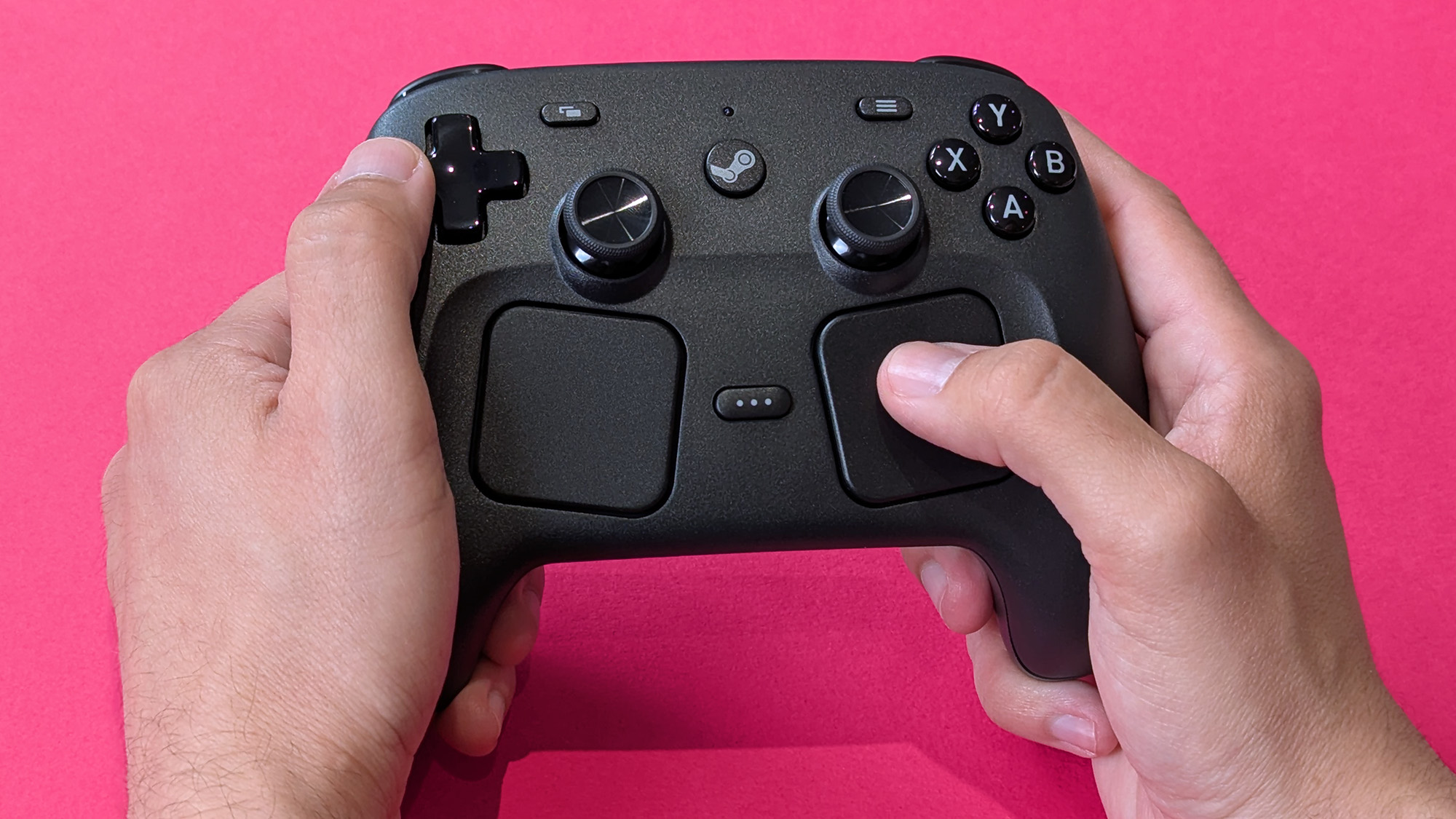 Valve Steam Controller (2026) held in two hands against a magenta card background
