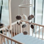 Stylish Scandinavian newborn baby nursery with natural wooden baby cot and handmade mobile hanging over it. Modern interior with white coloured walls, wooden furniture and indoor plants in the morning daylight. Getting ready for a new born! Welcome new born baby concept.