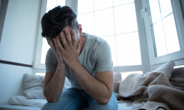 Young man sat on his bed with his head in his hands