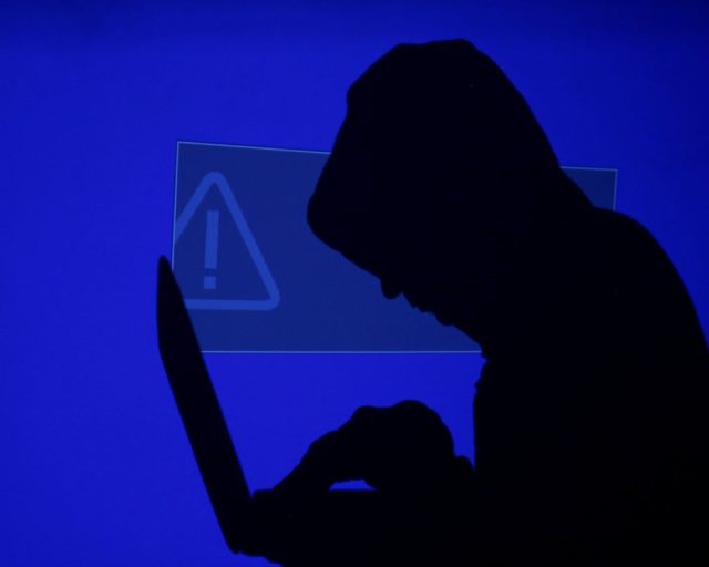 FILE PHOTO: A hooded man holds a laptop computer as blue screen with an exclamation mark is projected on him in this illustration picture taken on May 13, 2017. Capitalizing on spying tools believed to have been developed by the U.S. National Security Agency, hackers staged a cyber assault with a self-spreading malware that has infected tens of thousands of computers in nearly 100 countries. REUTERS/Kacper Pempel/Illustration/File Photo