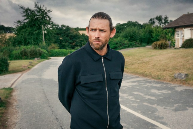 Chris Coghill as Kev Townsend in Emmerdale, posing in the middle of a village road and looking serious.