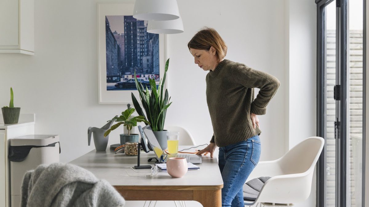 A mature woman (in her 40s) stands up whilst working from home. Her back twinges and she winces in pain. Poor posture/seating?
