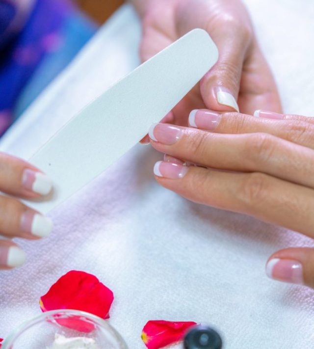 Closeup shot of a woman in a nail salon receiving a manicure by a beautician with nail file. Woman getting nail manicure. Beautician file nails to a customer.