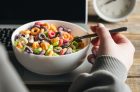 Woman eating colored breakfast cereal in front of laptop, workplace breakfast, quick healthy breakfast in office in the morning.