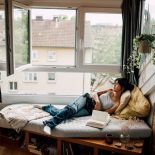 A serene moment of relaxation, with a person reclining by a window while reading in a comfortable, warmly-lit room adorned with decorative details.