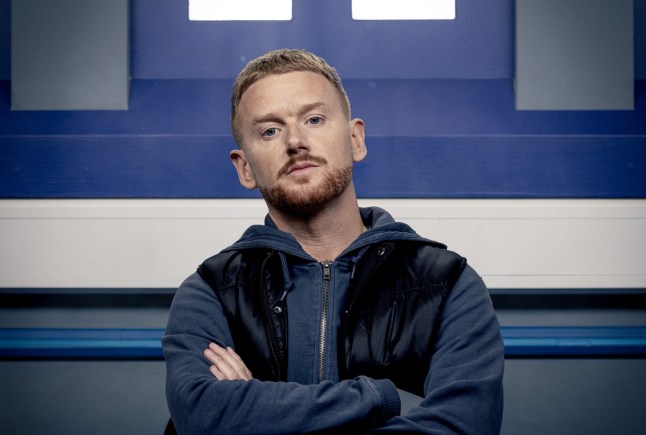Mikey North as Gary Windass, posing with his arms folded in a police station