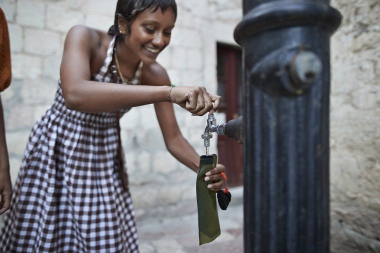 Smiling young woman filling water in bottle from faucet