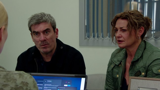 Cain and Moira sitting at a desk in a surgeon's office in Emmerdale