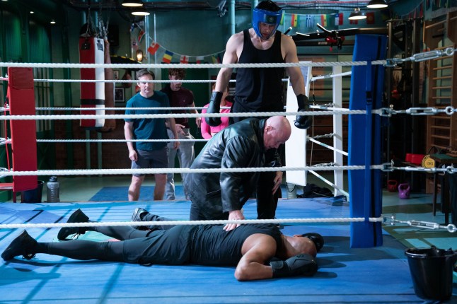 Mark Fowler standing over George Knight in a boxing ring while Phil Mitchell checks on him in EastEnders