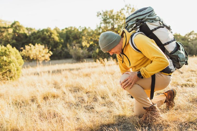 Man explorer stopping on way and suffering pain in knee while going hiking in autumn nature. Hiking, travel outdoor, recreation and active adventure concept. Success, travel, sport and motivational concept. Adventure and exploring nature.