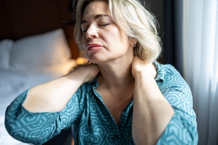 Tired woman wearing pajama and touching her neck with two hands, suffering from neck pain after sleeping on uncomfortable pillow