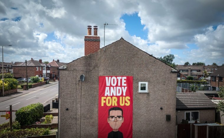ASHTON-IN-MAKERFIELD, ENGLAND - JUNE 13: An aerial view of a banner declaring "Vote Andy For Us" depicting Andy Burnham adorns the side of a home on June 13, 2026 in Ashton-in-Makerfield, England. The Makerfield by-election will take place on Thursday 18 June 2026 after Labour MP Josh Simons resigned to make way for Greater Manchester Mayor Andy Burnham to run giving him a route back to Westminster. While Labour won this seat at the 2024 general election with 45.2% of the vote to Reform UK's 31.8%, recent local council elections in May 2026 saw a shift, with Reform UK winning 49.8% of the area's vote compared to Labour's 24.3%. (Photo by Christopher Furlong/Getty Images)