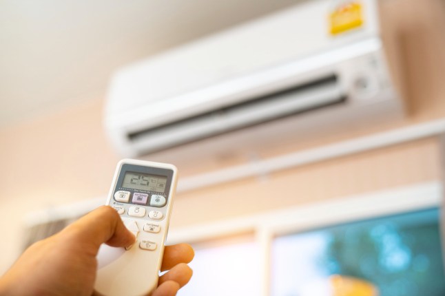A hand holds the remote control to switch on the air conditioning.