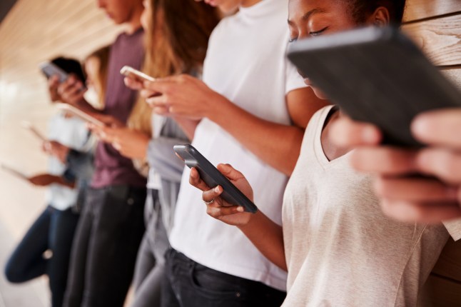 Teenagers standing against a wall, all using phones