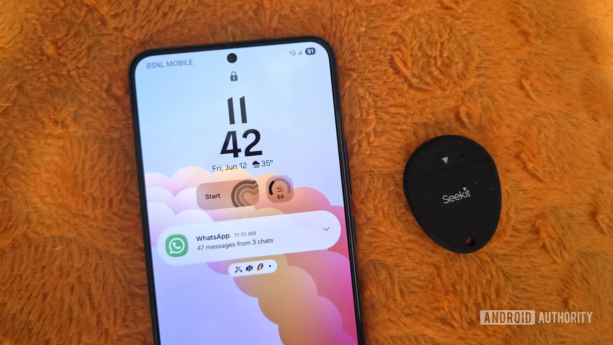 Samsung phone and a bluetooth tracker on an orange pillow