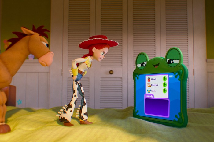 TOY STORY 5 A green frog tablet is on a bed while Jessie the cowgirl toy and her toy horse Bullseye, look at her angrily.