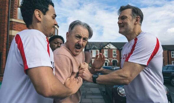 Men wearing football shirts grabbing at a man with a moustache