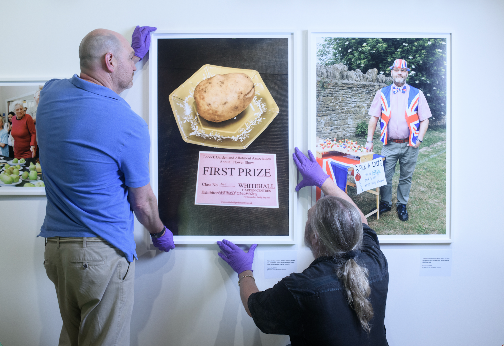 Two people stand looking at a large wall covered in rows of small contact-sheet style prints from the Lacock project.