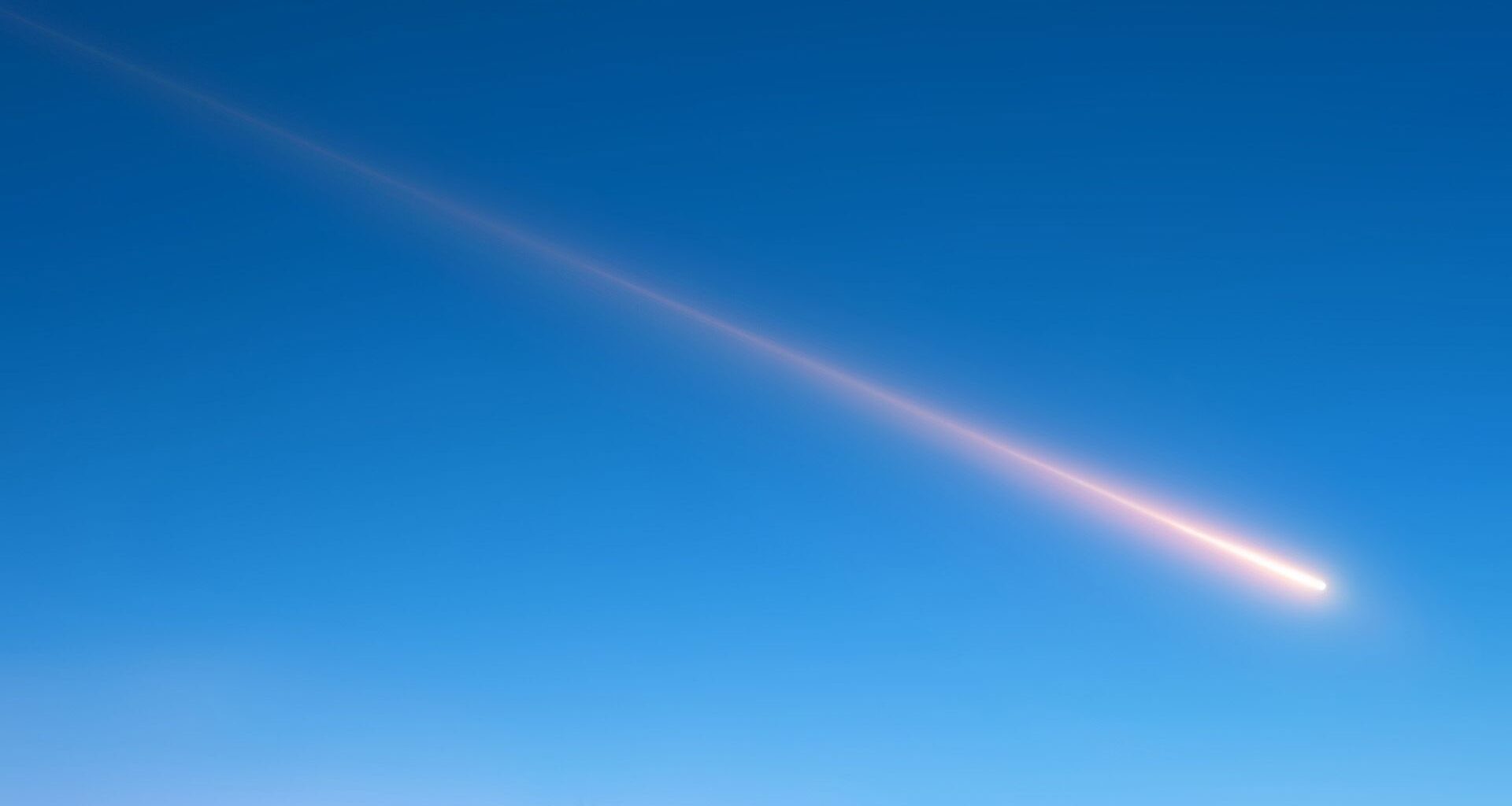 A streak of white moves across the blue sky as a meteor shoots past.