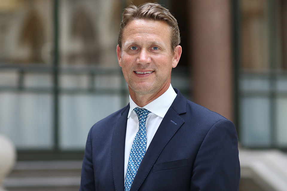 A professional portrait of Peter Vowles, the newly appointed British High Commissioner to Nigeria, wearing a navy blue suit and patterned tie, smiling outdoors.