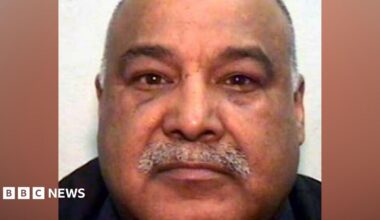 A mugshot of an Asian man in his 60s, with a grey moustache and bald head. He is looking into the camera.