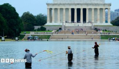 Workers with long poles clean the pool with the Lincoln Monument in the background