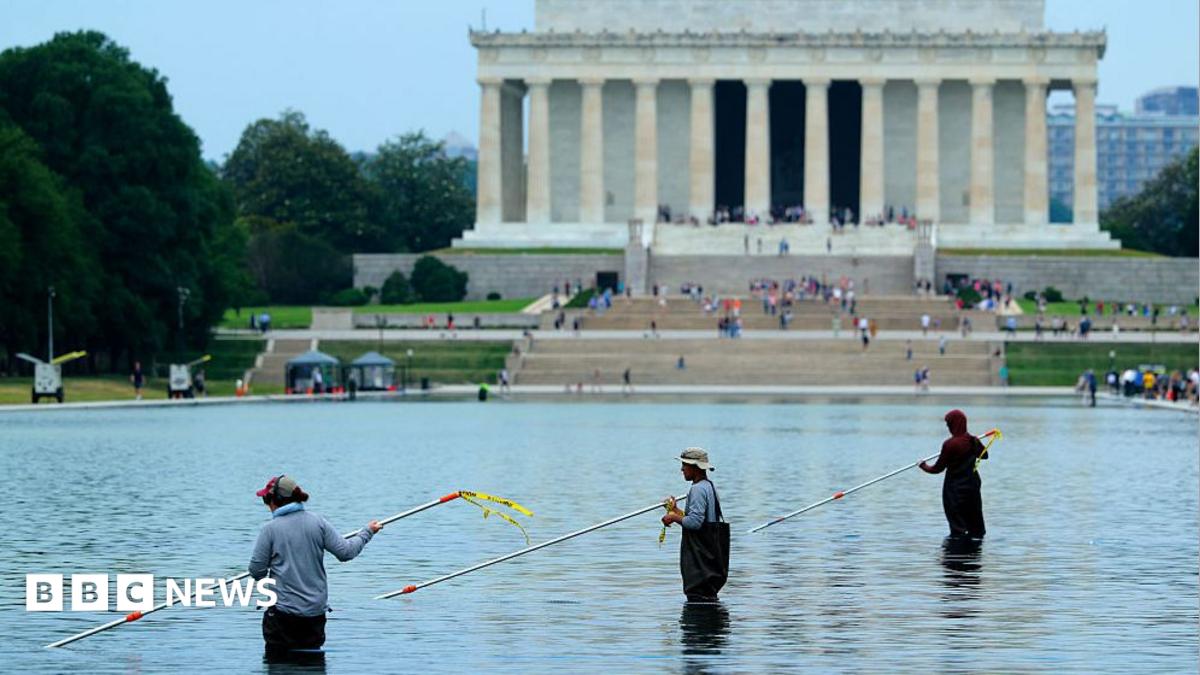 Workers with long poles clean the pool with the Lincoln Monument in the background