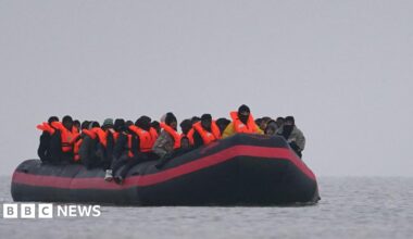 A small inflatable boat is on the water with a number of people wearing inflatable life jackets